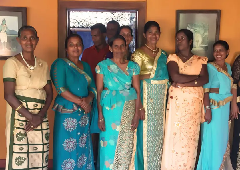 Mehrere Frauen in traditionellem Gewand "Sari" stehen vor einer Wand in orange