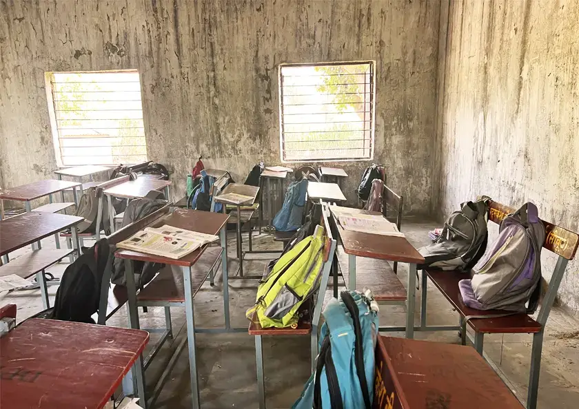 Aufnahme von einem leeren alten Klassenraum mit abgenutzten Tischen. An den Wänden blättert der Putz ab.
