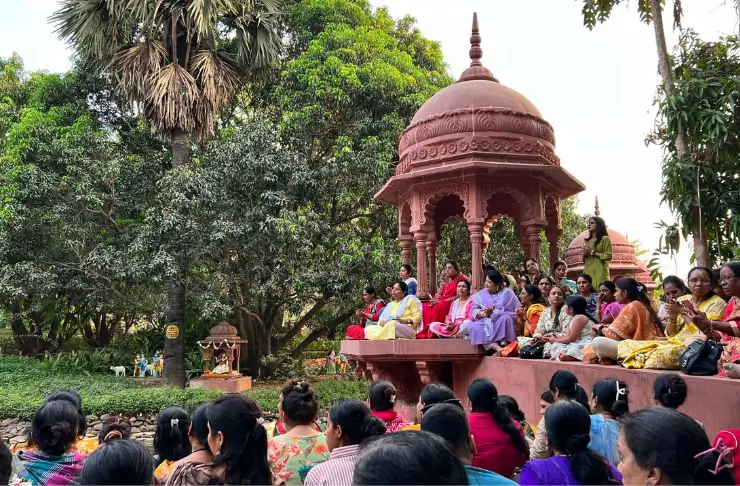 Indische Frauen und Männer sitzen in bunten Gewässern an einem Fluss und lauschen einer spirituellen Zeremonie