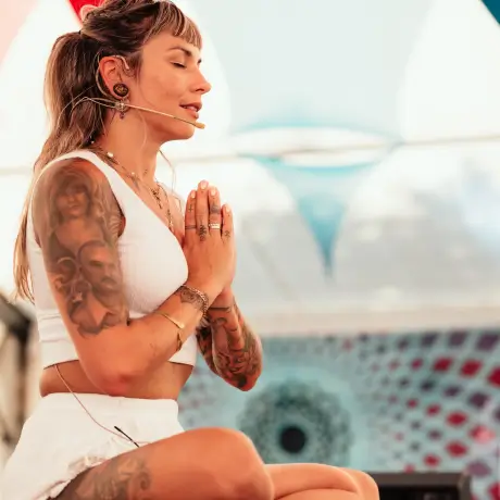 Yogalehrerin sitzt bei einem Yoga Festival, Hände in Gebetshaltung und Augen geschlossen.
