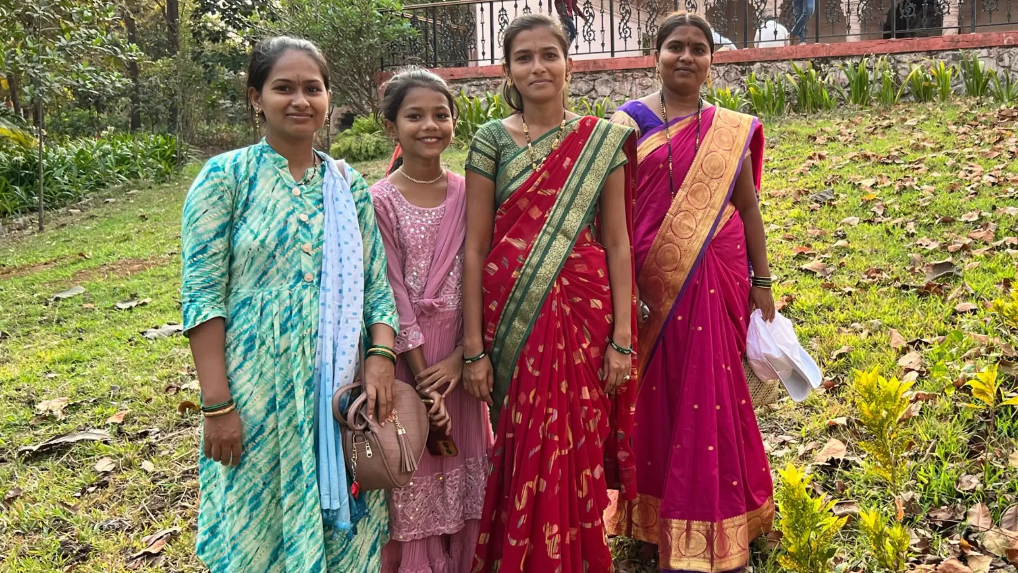 4 indische junge Frauen stehen in ihren bunten Gewändern vor einem Tempel und lächeln in die Kamera