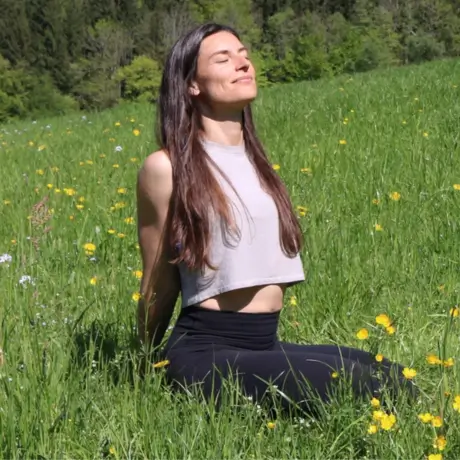 Yogalehrerin Susanne kniet im Gras und streckt den Kopf in Richtung Sonne