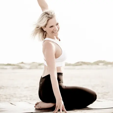 Yoga Lehrerin für Retreats Kristina sitzt im Fersensitz am Strand und hebt den linken Arm