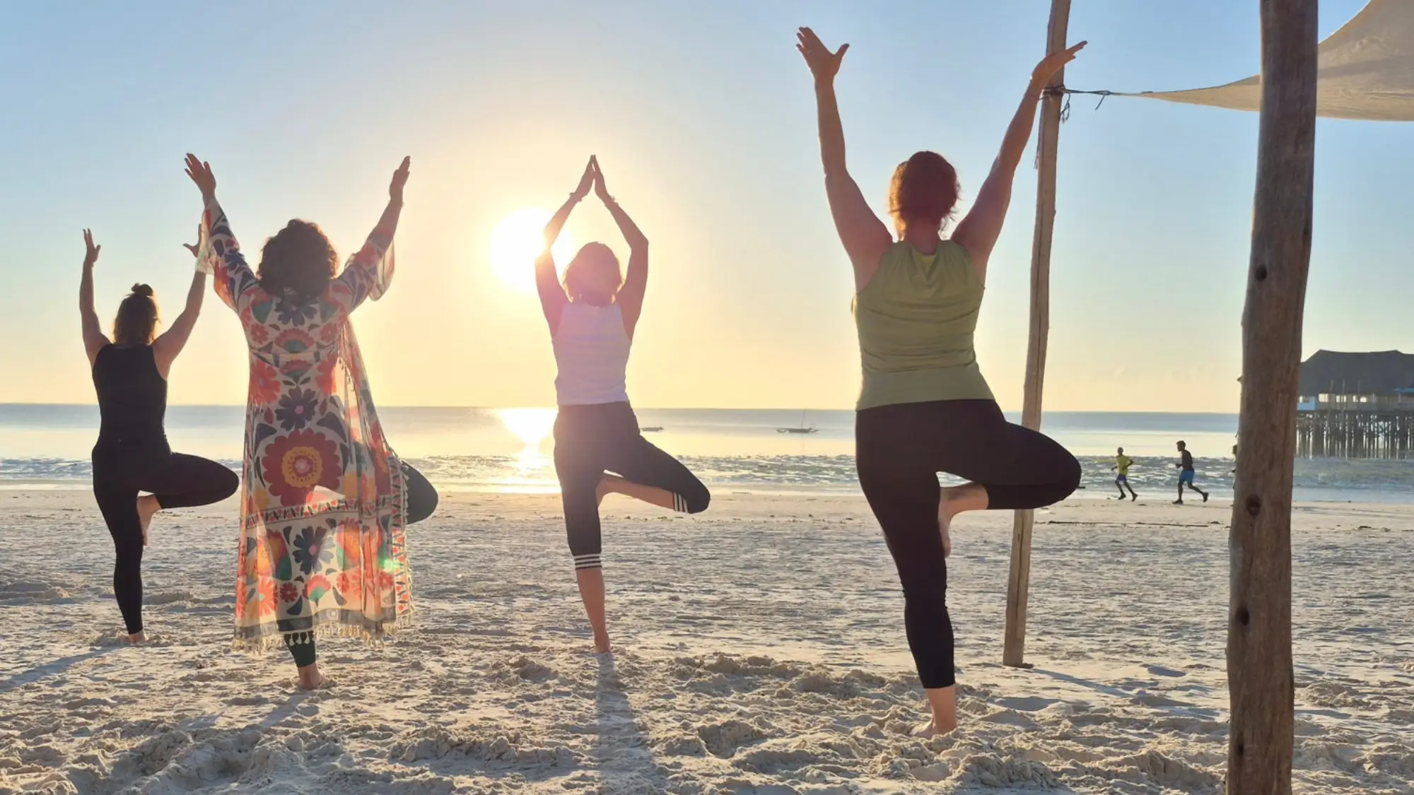 Teilnehmerinnen beim Sansibar Yoga Retreat machen morgens Yoga am Strand beim Sonnenaufgang